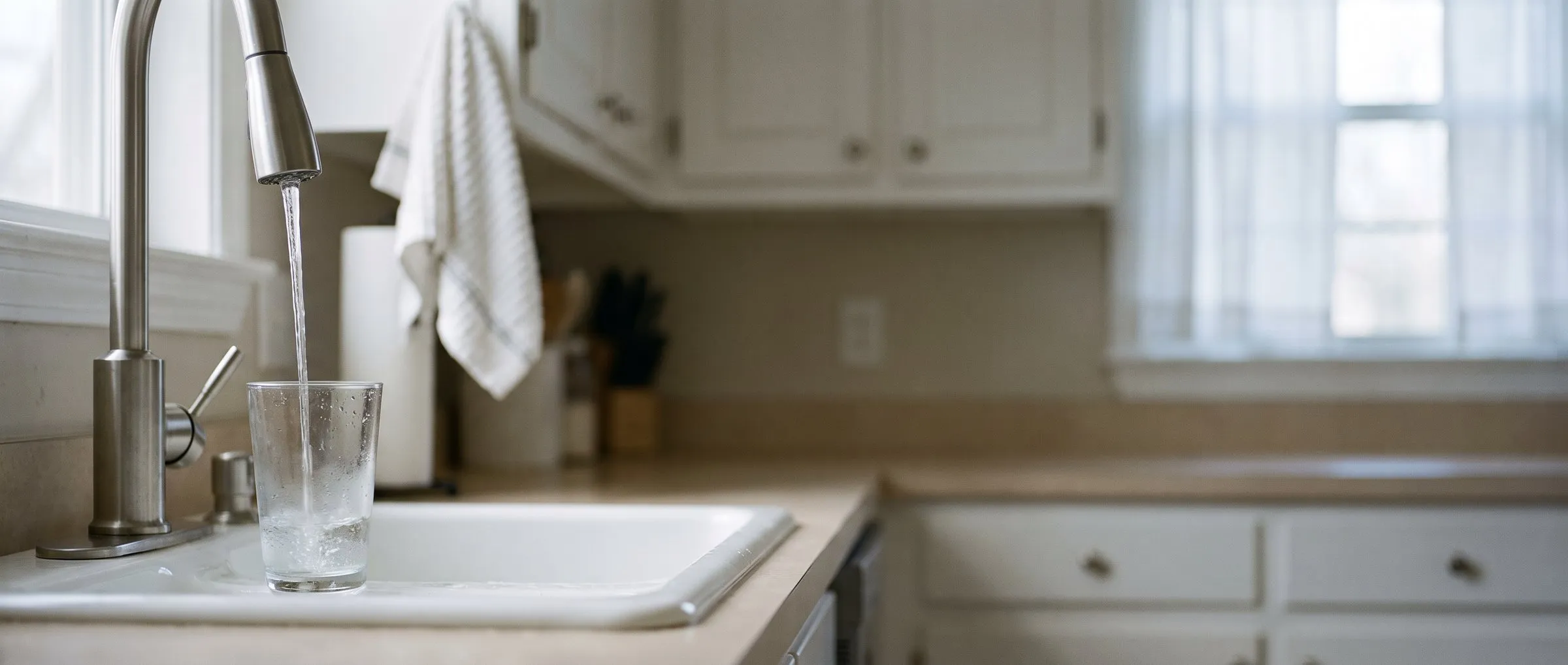 A glass filling with water at a bright kitchen sink in morning light.