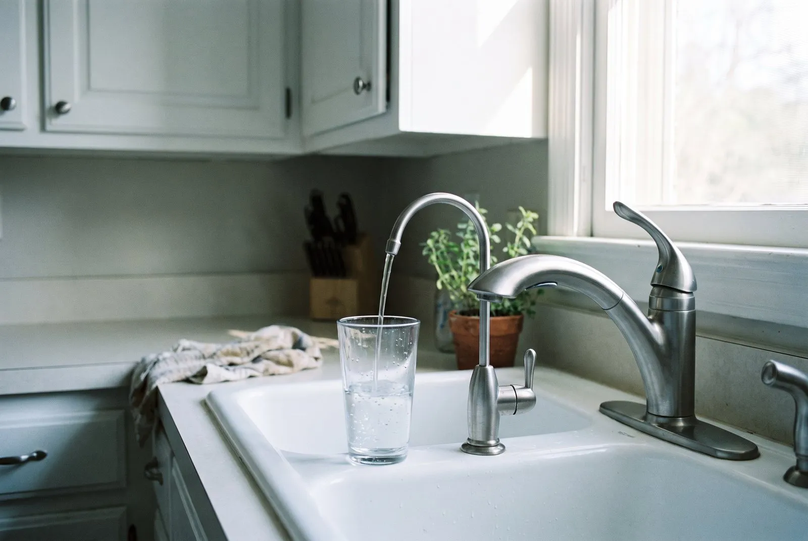 A small drinking-water faucet beside a kitchen sink, filling a drinking glass.